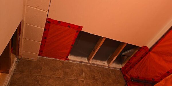 A room with partially exposed walls showing insulation and wooden studs, possibly undergoing mold remediation in Richmond Hill. Orange vapor barrier and red tape cover some sections, brown floor tiles are visible, and the upper walls are painted light peach.