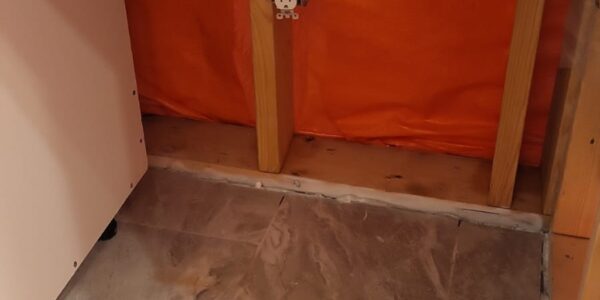 A section of wall with exposed studs and orange insulation, featuring an electrical outlet and a large power socket; ideal for Mold Remediation Oakville projects. The floor is covered with light gray and beige tiles.