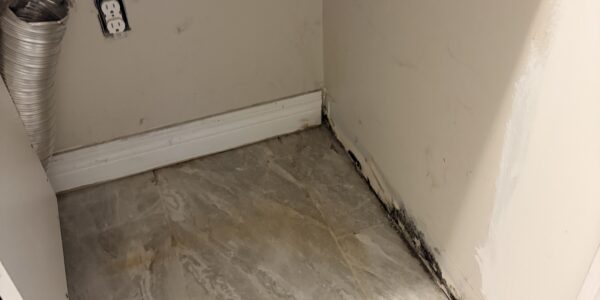 A corner of a room with a tiled floor, exposed wall outlet, vent hose, and visible black mold along the base signals a need for professional Mold Remediation Oakville services.