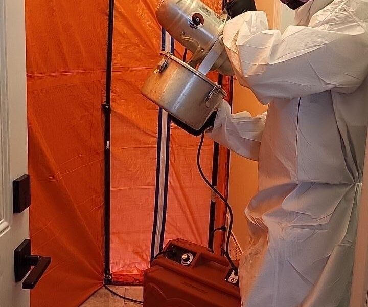 Mold remediation technician wearing protective equipment performing fogging treatment inside a contained laundry room remediation area in Oakville.