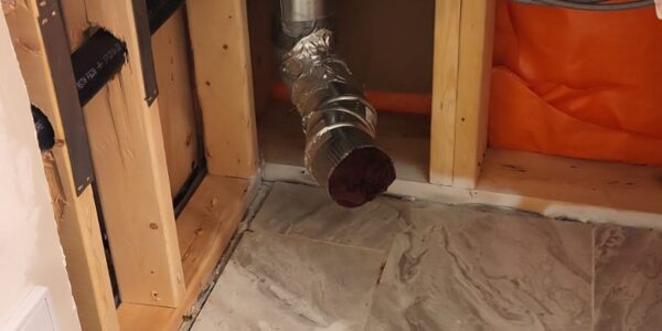Exposed pipes and ducts inside a wall with missing drywall, wooden studs, and insulation visible—ideal for a Mold Remediation Oakville project; gray tile flooring in the foreground.
